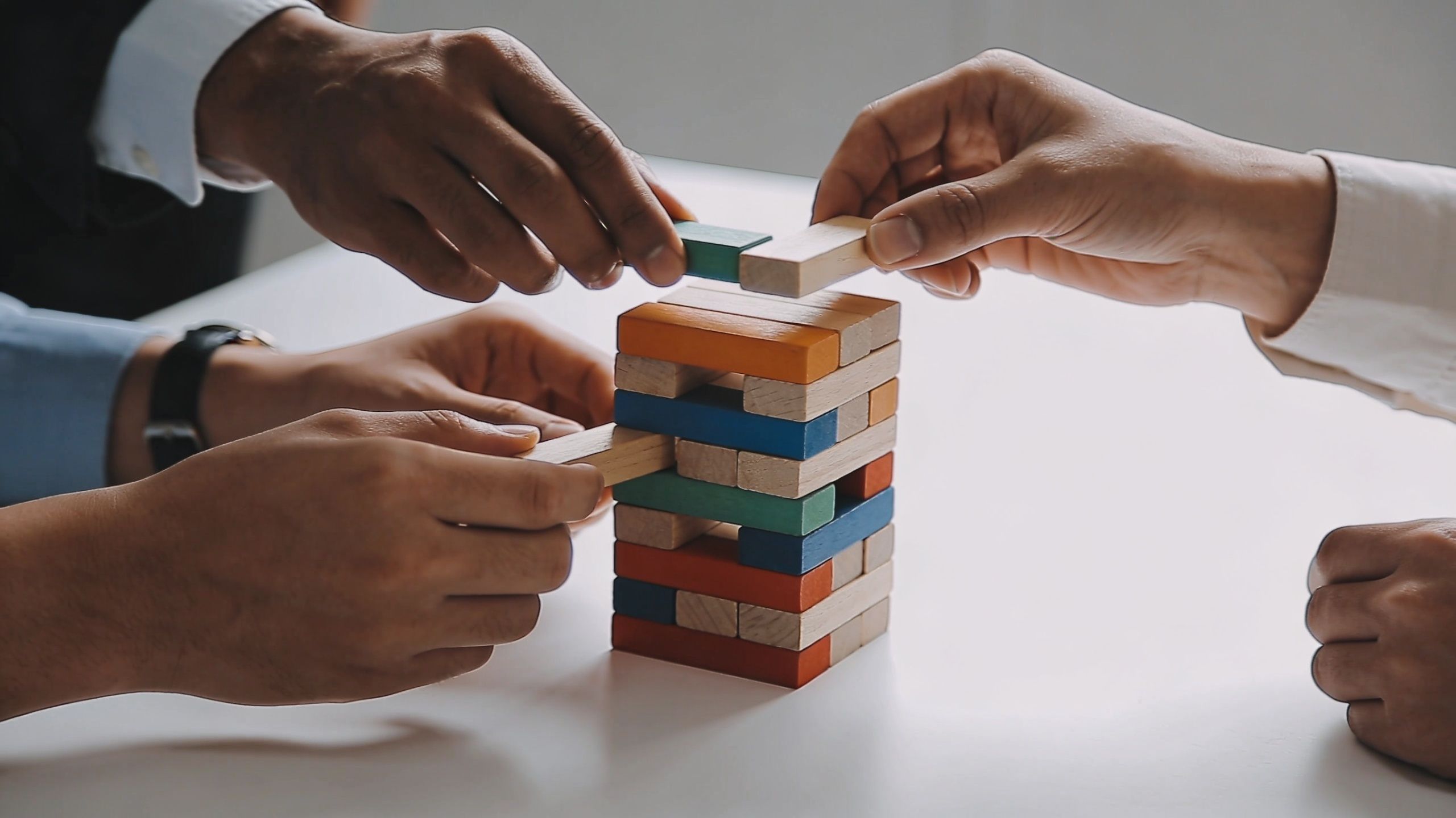 A diverse business team collaborating to build and balance a colorful wooden block tower on a table.