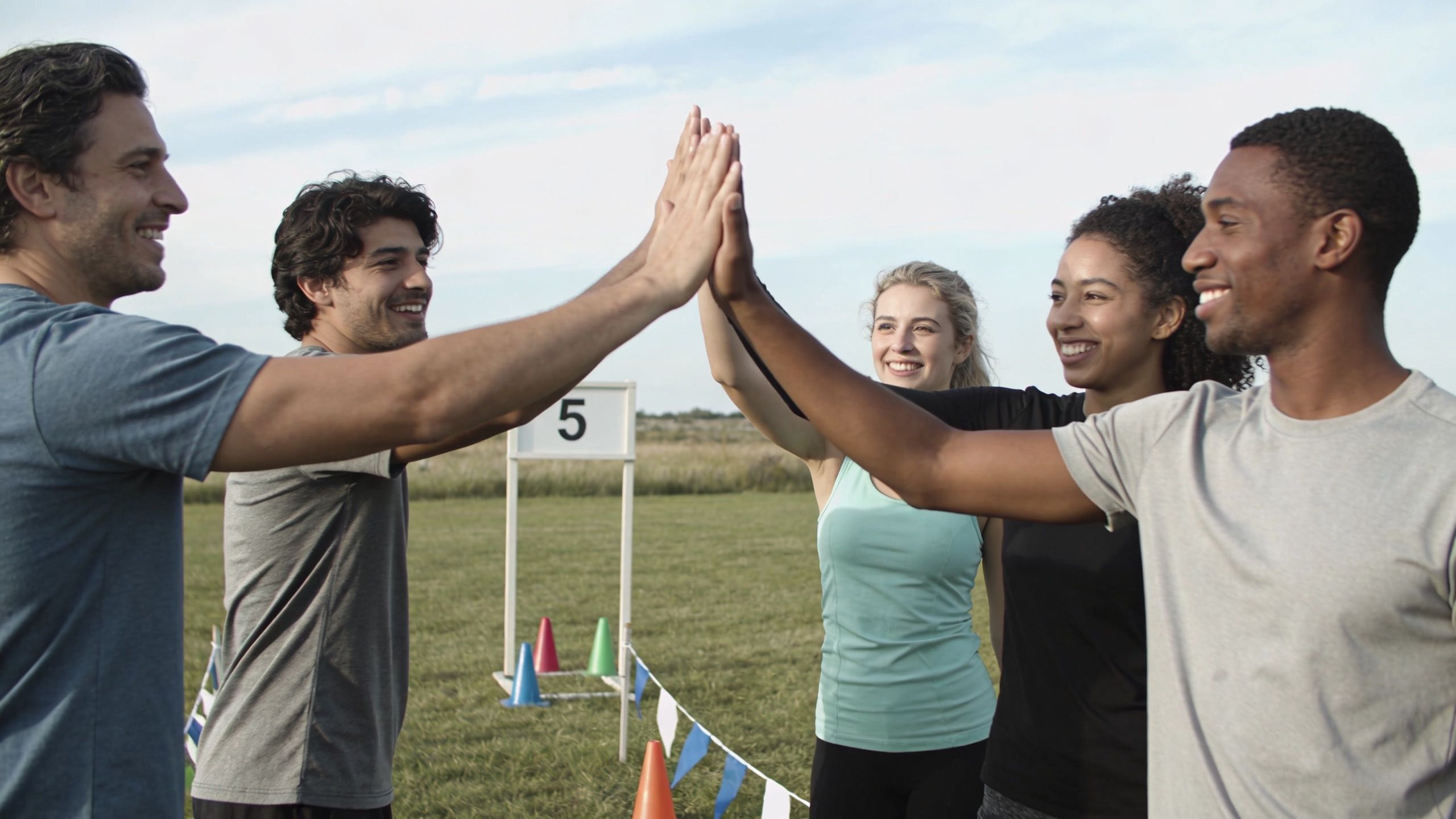 A diverse group of cheerful adults sharing a high-five during an outdoor team building activity on grass.