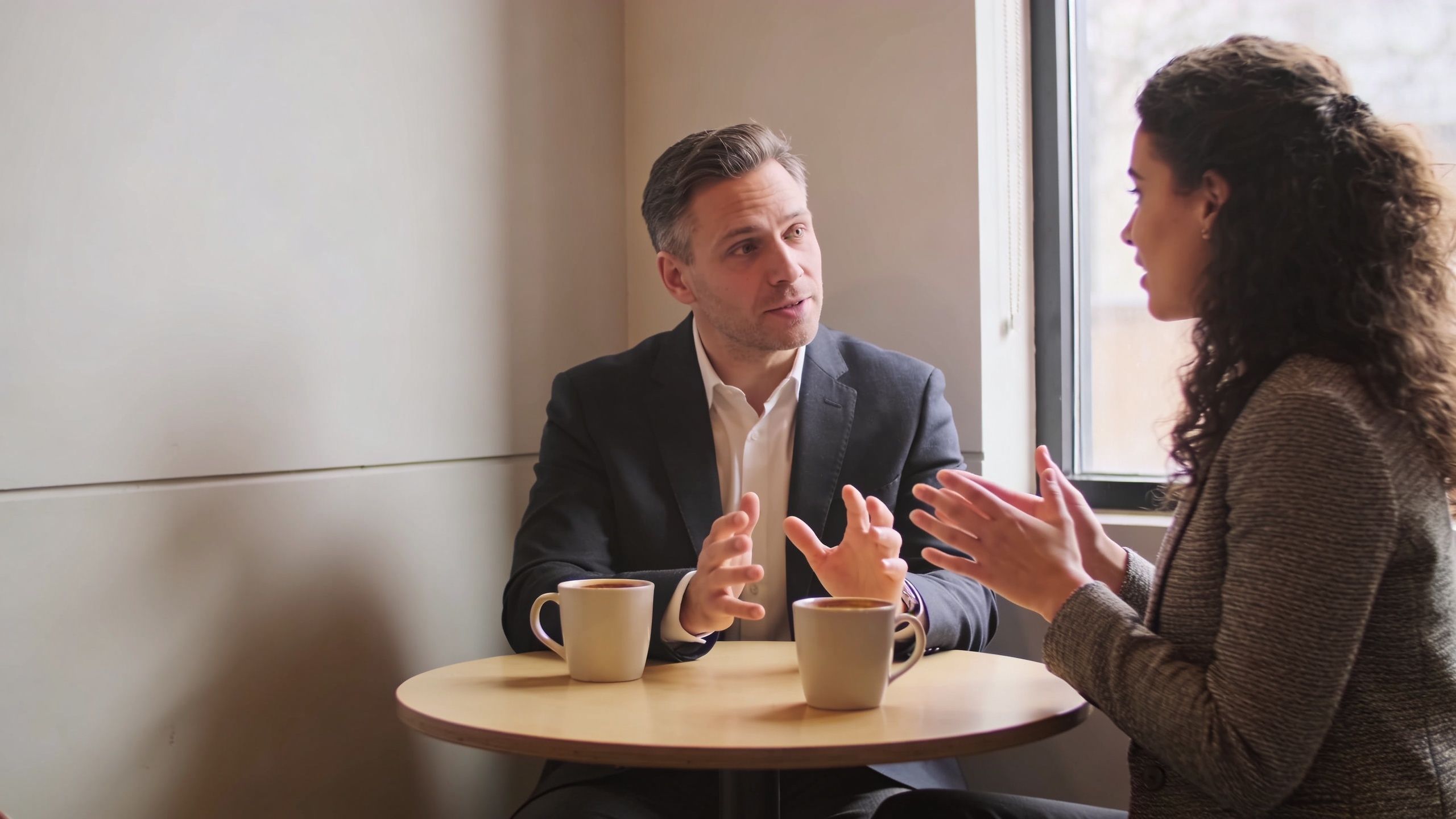 A professional man and woman having a conversation over coffee in a bright office space.