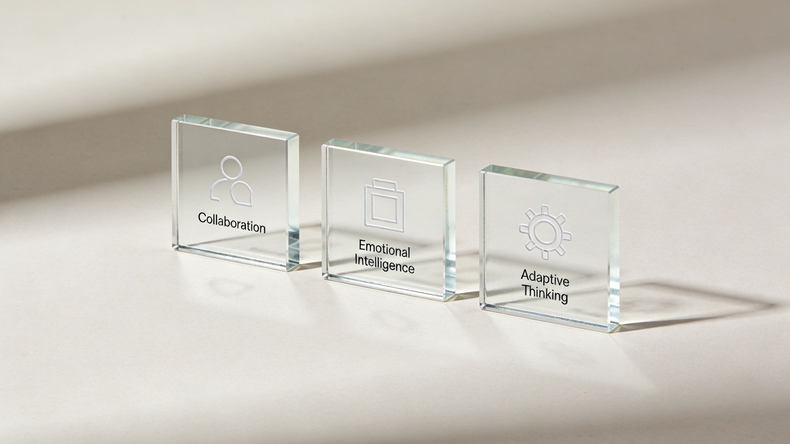 Three glass cubes on a neutral surface representing professional development concepts of collaboration, emotional intelligence, and adaptive thinking.