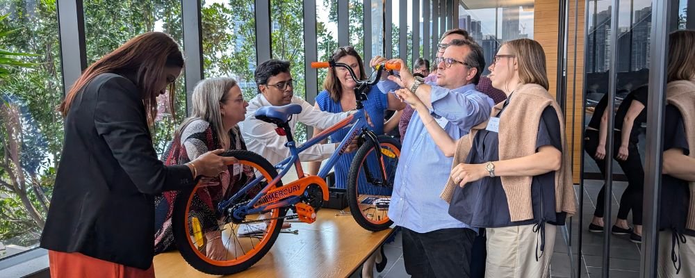 Diverse team cooperatively assembling a blue and orange bicycle during a team-building event.