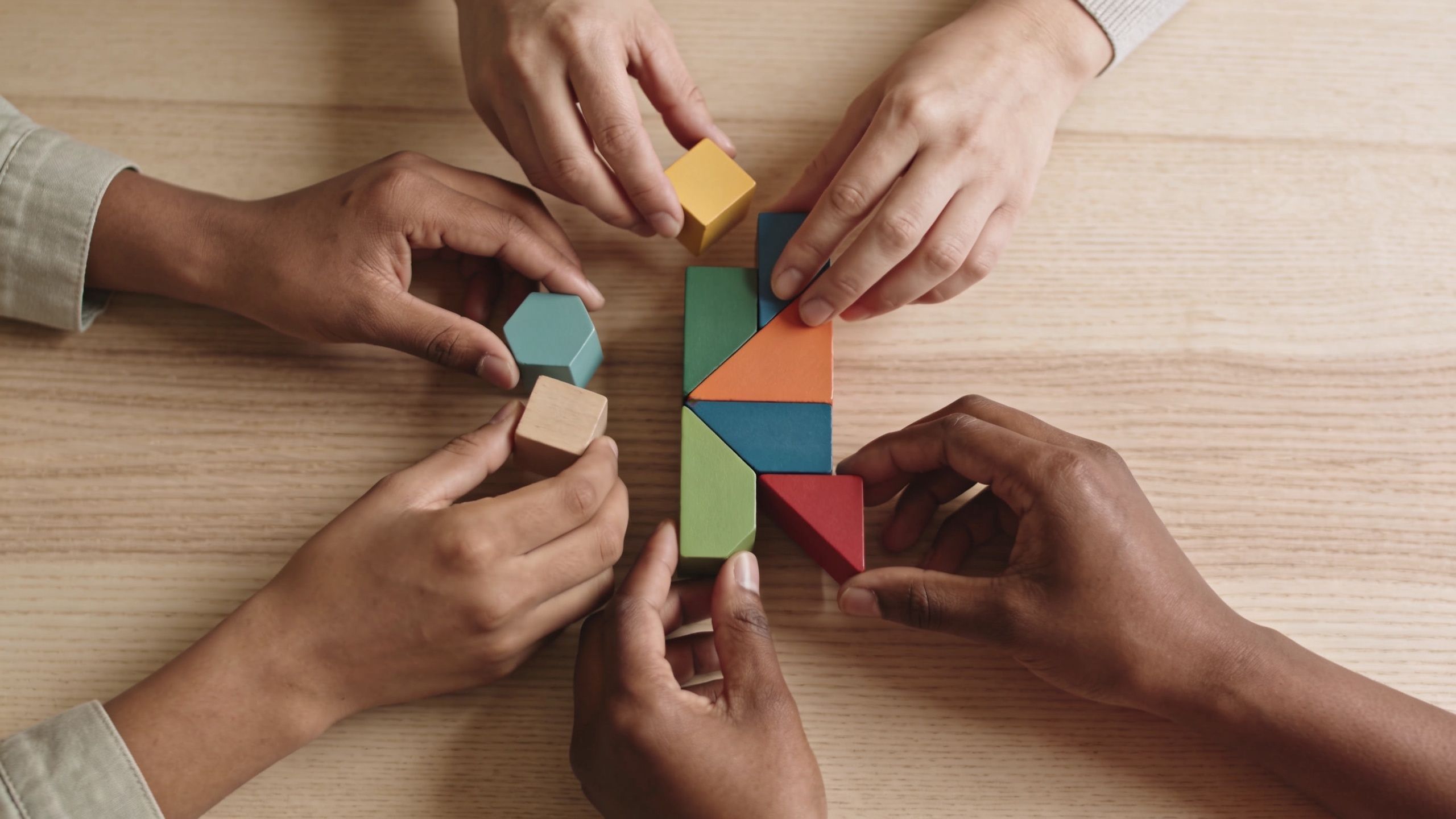 A diverse group of people collaborating together by assembling colorful wooden geometric puzzle blocks on a table.