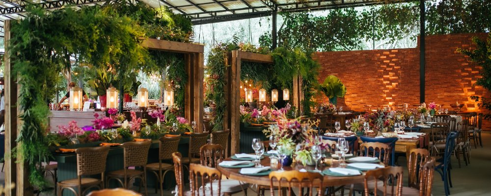 A luxurious event space decorated with abundant greenery, colorful flowers, and elegant dining tables under warm lights.