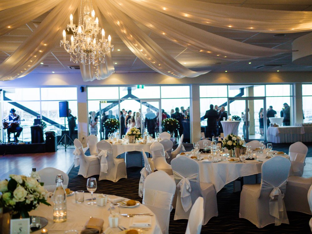 A beautifully decorated event hall with dining tables, a musician on stage, and guests mingling.