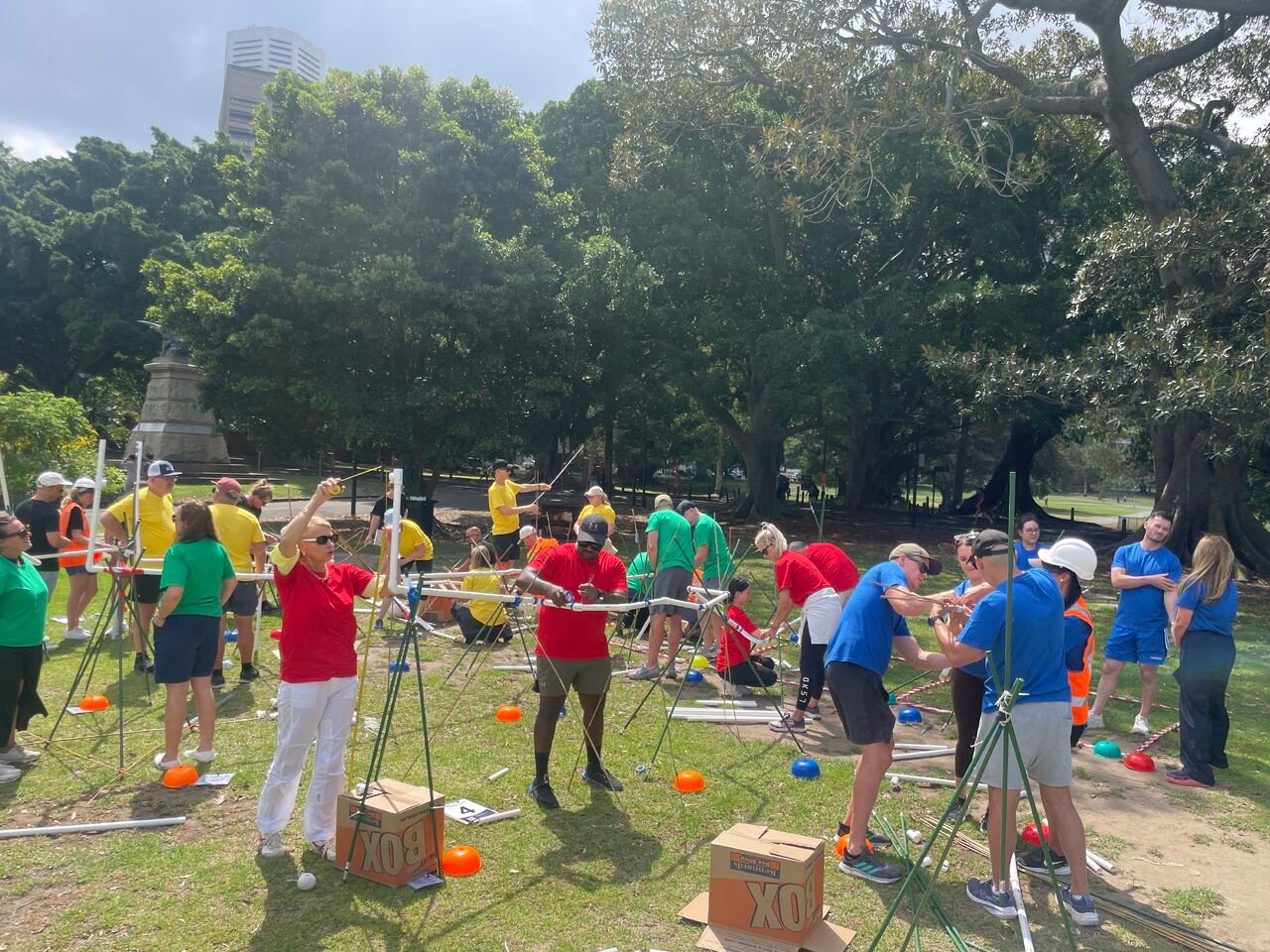 A diverse group of people participating in a collaborative outdoor team building activity in a park.